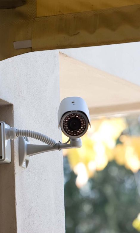 An exterior view of a commercial building outfitted with multiple security cameras mounted on its façade, with visible wiring and an urban backdrop.