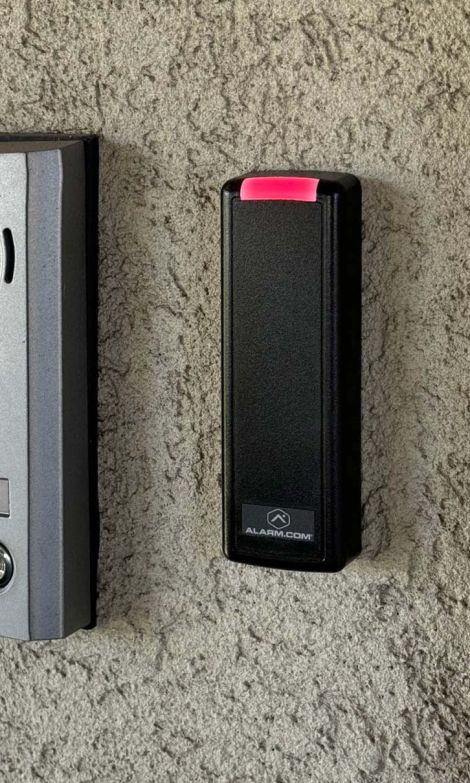 A black and red Alarm.com access control scanner mounted on a wall in an entryway.