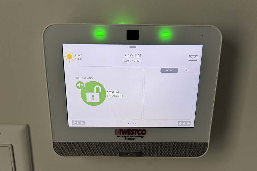 A Westco Security touchscreen control panel mounted on a wall displaying a disarmed status and green LED indicator lights.