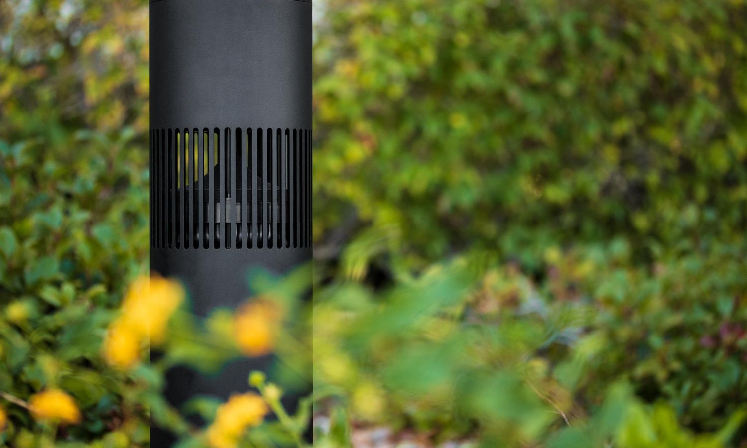 A modern outdoor landscape speaker partially hidden among plants and flowers, designed to blend into the garden while delivering outdoor audio.