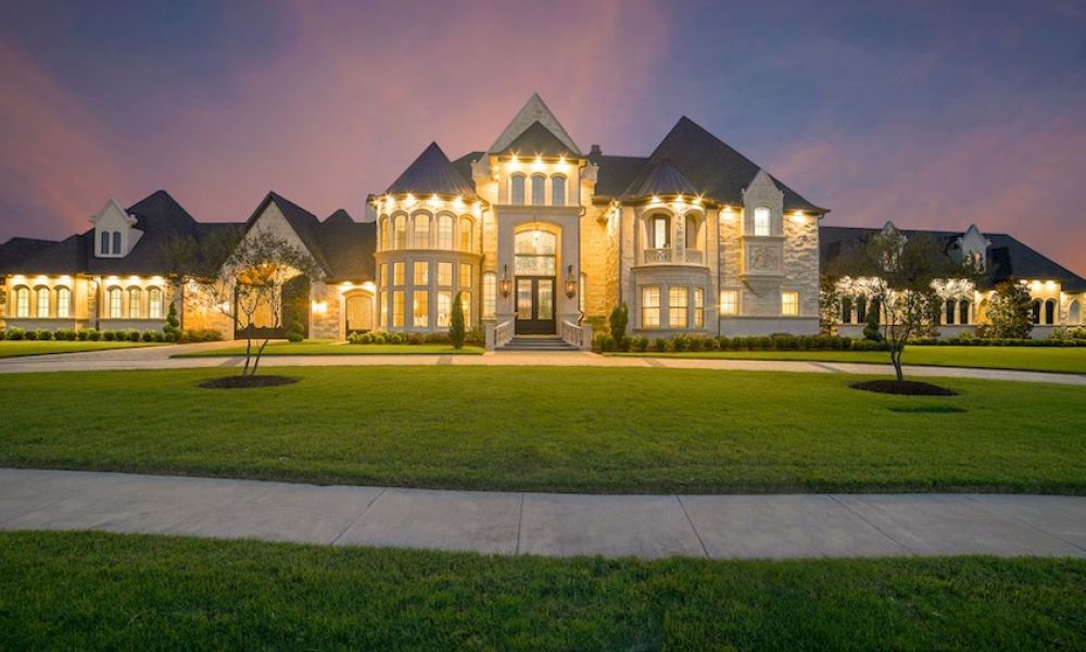 Elegant luxury home with an expansive footprint and lawn, lighted at night.
