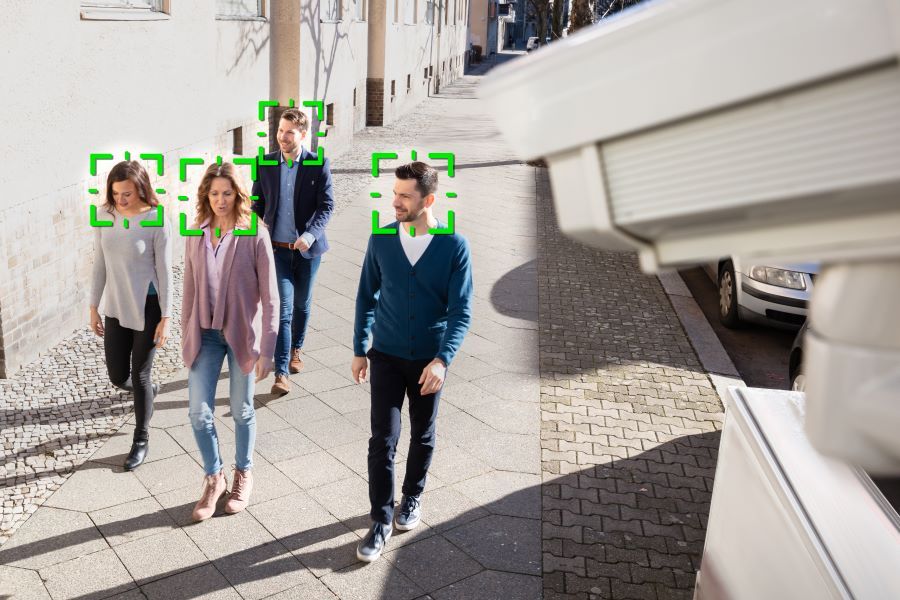 People walking on a sidewalk under video surveillance and facial recognition.