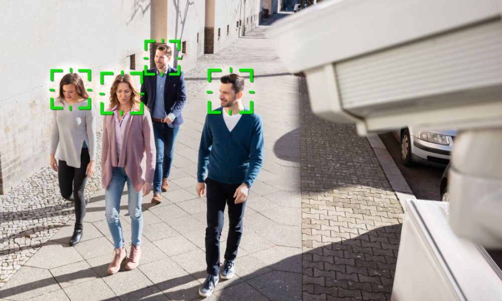 People walking on a sidewalk under video surveillance and facial recognition.