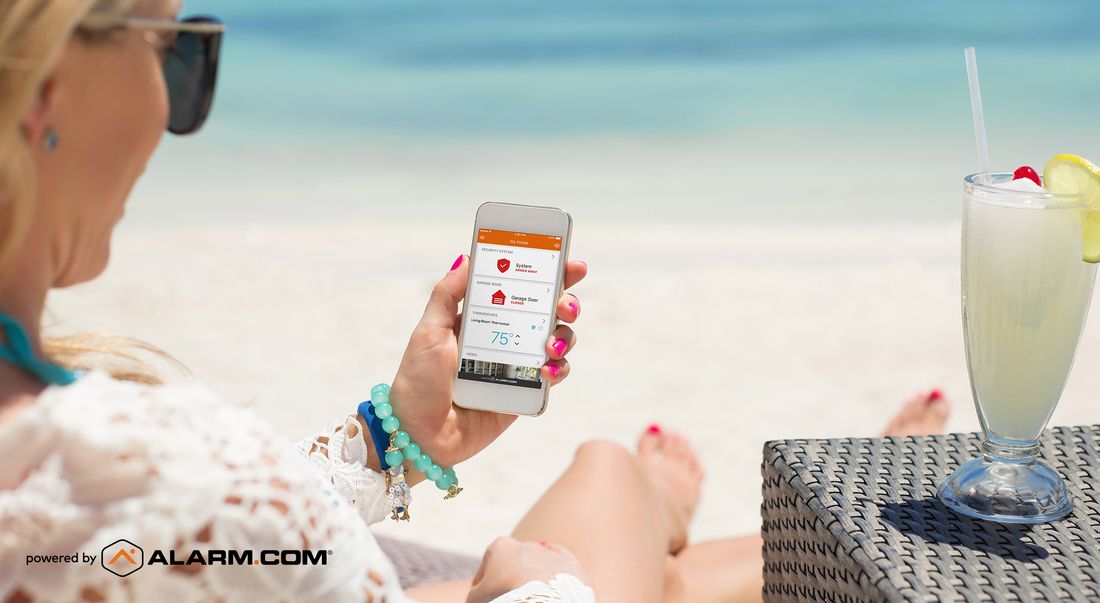 Woman relaxing on a beach chair using the Alarm.com mobile app on her smartphone to monitor home security.