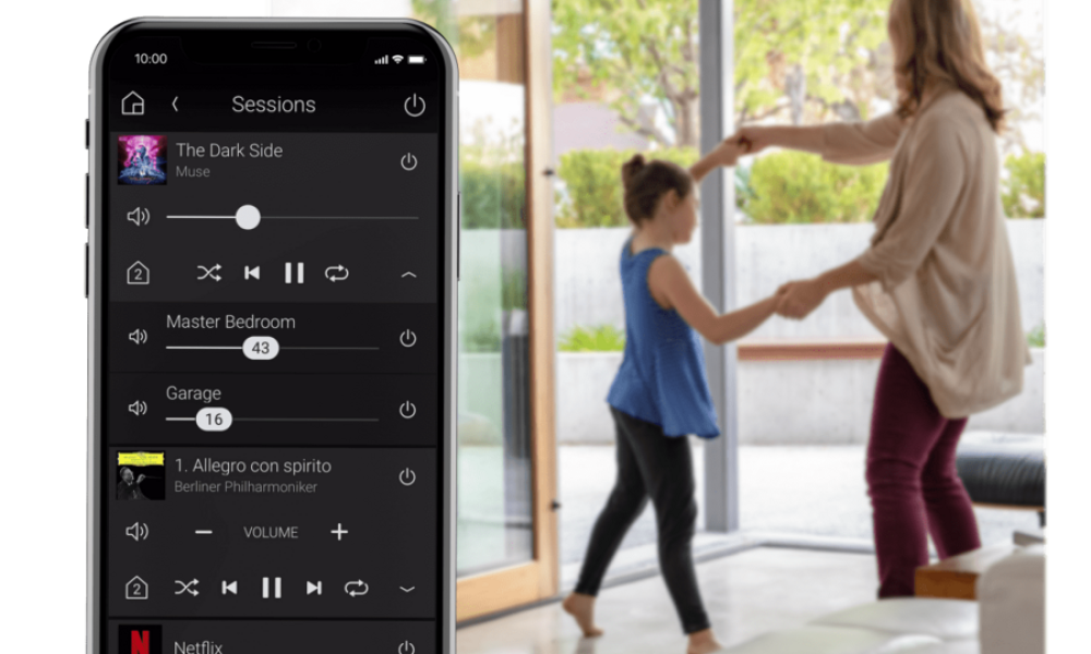 A phone displays the entertainment platform of the Control4 app while overseeing a mother and a daughter dancing happily.