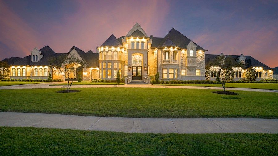 Elegant luxury home with an expansive footprint and lawn, lighted at night.